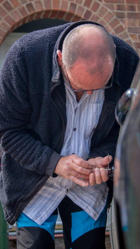 locksmith-lockpicking-a-car-17124739 A auto locksmith works on unlocking a car, demonstrating his expertise and tools.